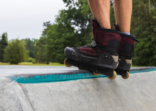 Rear close-up of aggressive inline skates on a mature man balancing on a concrete ramp edge at a skatepark