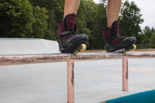 Front close-up of aggressive inline skates on a mature man performing a frontside grind on a metal rail