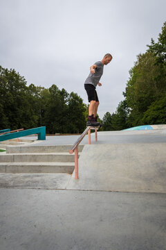 Vertical shot of a mature man performing an aggressive inline skate grind trick on a rail at a skatepark
