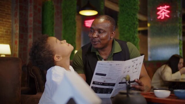 Black father and son reading menu in cozy cafe