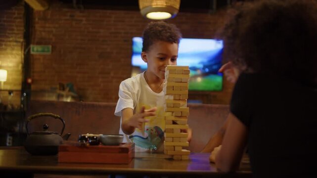 Father watching son build wooden block tower with daughter in cafe