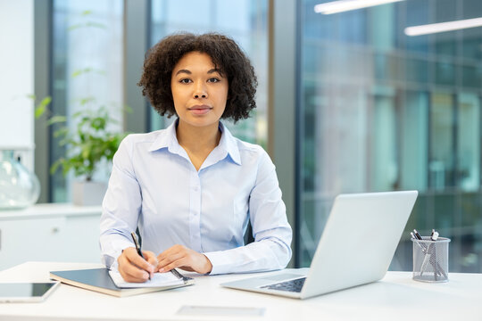 Portrait of a serious young African American businesswoman sitting at her desk in the office. Holding a pen and looking at the camera