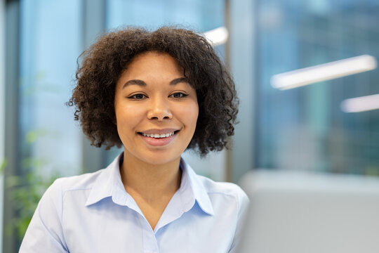 Smiling young African American woman sitting in front of laptop in office and looking at screen