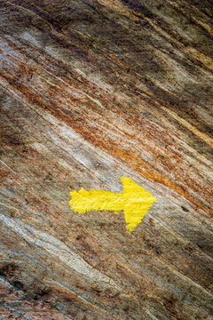 A painted yellow arrow on the rock is pointing the way in the Italian Alps