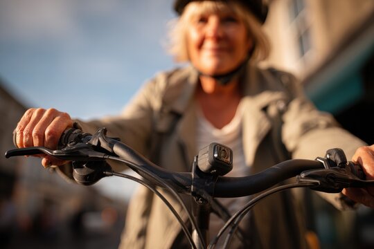 Senior woman riding bicycle in city. Active lifestyle of elderly female cyclist with helmet. Healthy retirement activity and urban transportation for older adult concept at sunset.