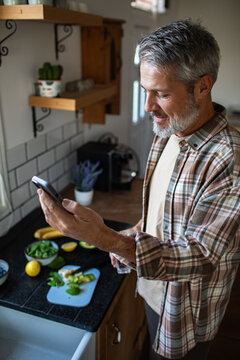 Middle-aged man using smartphone for recipe in home kitchen