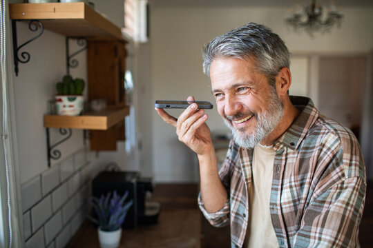 Smiling middle-aged man using voice assistant in home kitchen