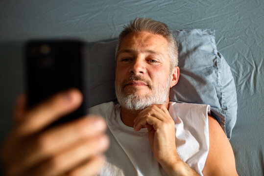 Middle-aged man using smartphone in bed at home