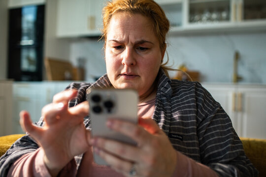 Middle-aged woman checking smartphone in home kitchen