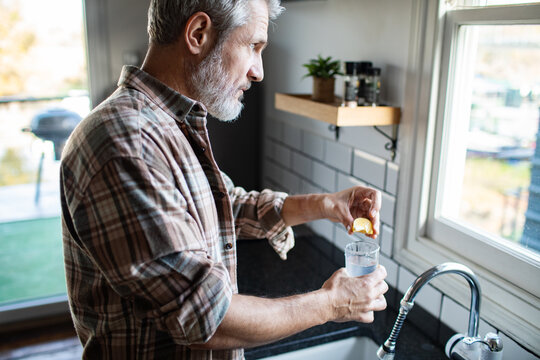 Mature man squeezing lemon into water at home kitchen sink