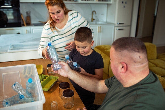 Parents and child sorting plastic bottles for recycling in home kitchen