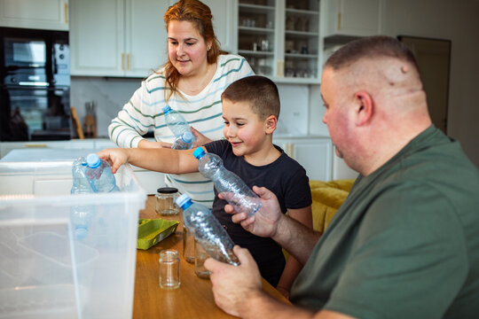 Parents and child sorting plastic bottles for recycling in home kitchen