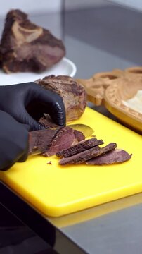 Chef in black gloves slicing tender boiled beef meat with a sharp knife on a bright yellow cutting board, slow motion vertical video.