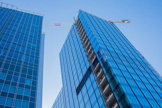 Two glass skyscraper buildings and building crane near them with the background of blue sky low angle view. Modern business office building architecture, construction, big city life