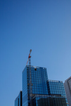 Modern tall skyscraper building with a building crane near on the last stage of building with the background of clear blue sky and copy space