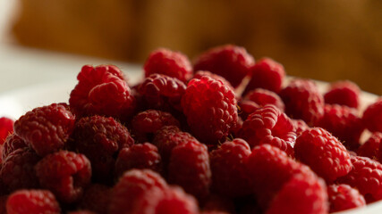 Human hand holding a fresh red raspberry on an open palm over a white bowl filled with ripe berries. © kyrylovasyliev