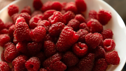 Extreme close-up of fresh red raspberries in a white bowl under warm natural sunlight. © kyrylovasyliev