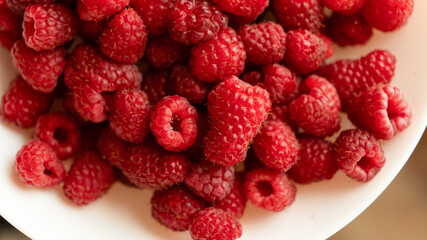 Extreme close-up of fresh red raspberries in a white bowl under warm natural sunlight. © kyrylovasyliev