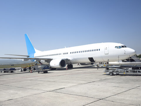 View of a white passenger airplane parked on the tarmac at Kars Airport with ground support equipment nearby under a clear blue sky in Kars, Kars, Turkiye.