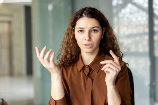 Professional young businesswoman with curly hair talking and actively gesturing with her hands while communicating during a meeting in a modern office environment