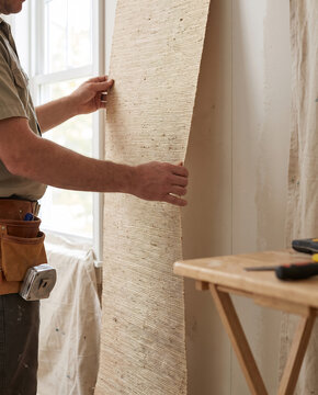 Installer holding a grasscloth wallpaper panel against a wall for dry-fit alignment