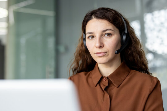 Woman wearing a headset and brown shirt, looking forward while providing customer support at a telemarketing call center desk