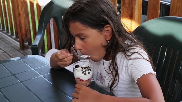 Girl eating dessert parfait at outdoor patio table in summer