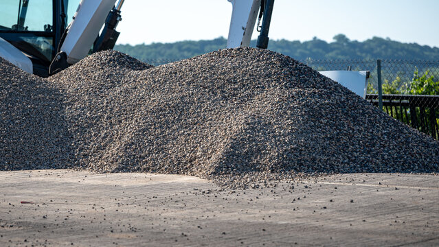 massive pile of gray crushed stone gravel at an active outdoor construction site with excavator in the background on a bridge area. infrastructure concepts.