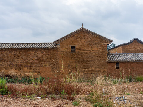 Historic mud brick building gable wall with dry wild weeds foreground
