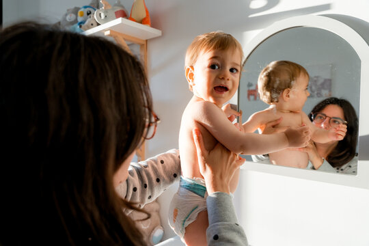 Mother holding baby in front of mirror during diaper change