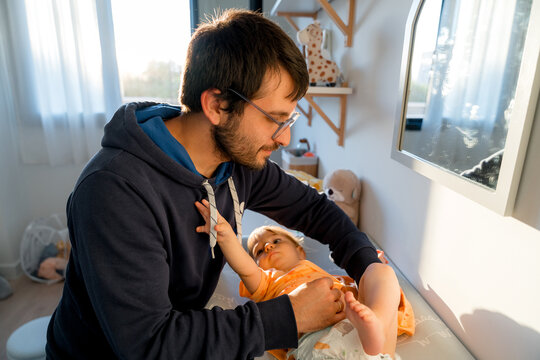 Father changing baby diaper in nursery with warm sunlight