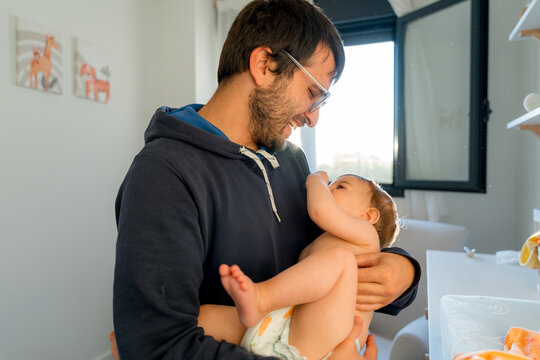 Smiling father holding baby at home in warm window light
