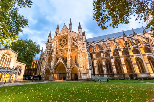 View of the historic Westminster Abbey with its intricate Gothic architecture, rose window, and stone facade set against a green lawn in London, England, United Kingdom.