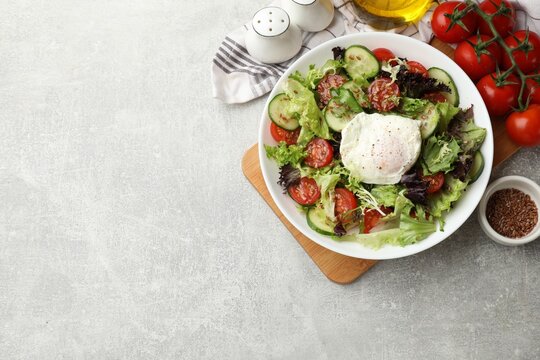 Delicious vegetable salad with poached egg in bowl and ingredients on gray textured table, flat lay. Space for text