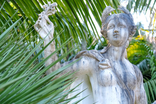 Weathered stone statue framed by tropical palm leaves