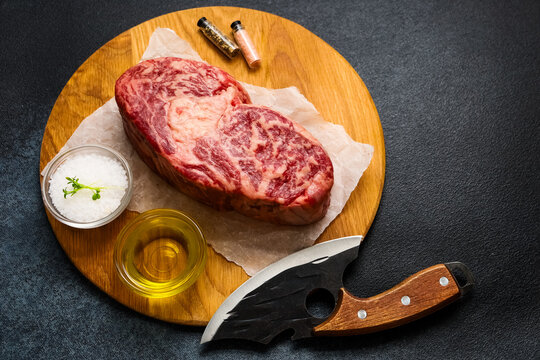 Beef steak preparation on a wooden board with olive oil and seasoning on the side