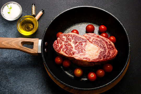 Cooking a steak with cherry tomatoes in a frying pan on a dark countertop
