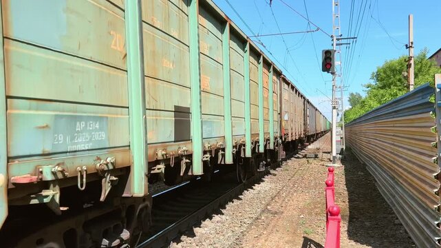 Freight train wagons passing rusty metal fence with electric power lines