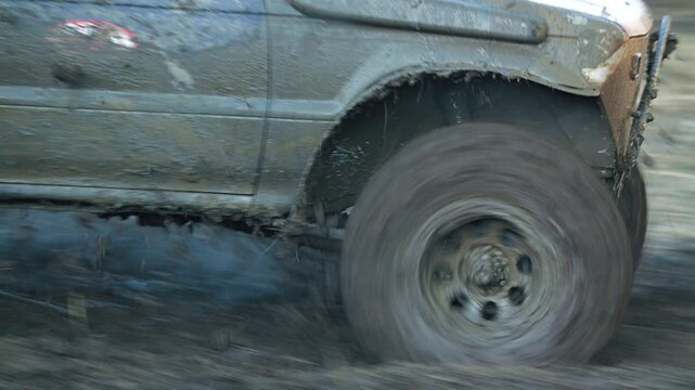 Close up action shot of dirty four wheel drive vehicle. Spinning tire splashing mud. Dynamic composition captures extreme motorsport and adventure. Earthy tones dominate