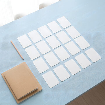 Overhead view of blank white flashcards arranged in a grid on a pastel blue desk with pencil