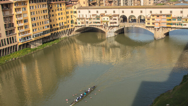 View of the historic Ponte Vecchio bridge spanning the Arno river with a rowing boat moving through the water in Florence, Tuscany, Italy.