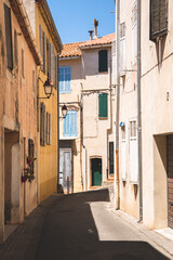 Fototapeta premium A gentle curve in a narrow European alleyway reveals historic multi-story buildings painted in warm pastel hues. Colorful wooden shutters in blue and green contrast against the sunny facade, evoking c