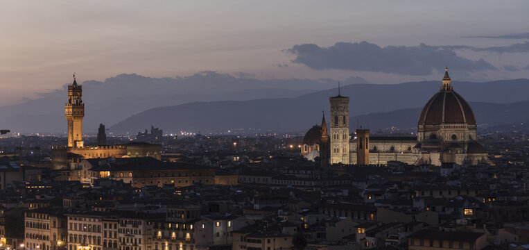 View of the Florence Cathedral, Giotto's Campanile, and Palazzo Vecchio illuminated at dusk over the historic city skyline in Florence, Tuscany, Italy.