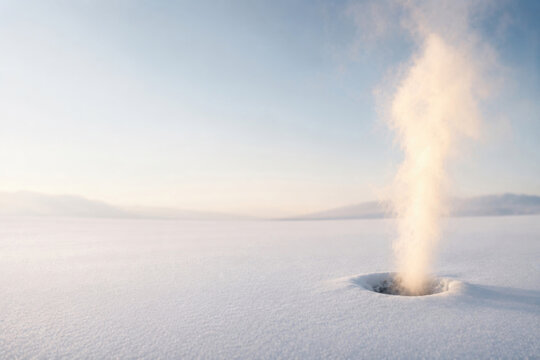 Steam rises from a hole in a snowy landscape. Space for text.