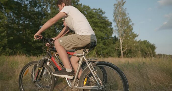 Two boys riding bicycles on nature. Teenagers spending time together. 4K 10-bit