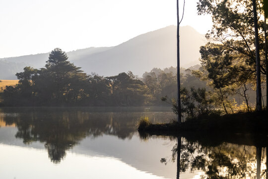 Ethereal gold and pale blue landscape reflecting in the calm waters of the Hippo pool with the distant peak of Nyonyane Mountain, hazy in the background in Mlilwane Wildlife sanctuary, Eswatini.