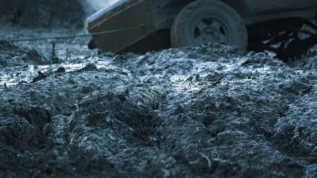 Low angle close up of thick, wet mud churned by off road vehicle. SUV in background with tow cable. Cool, blue tones create gritty, adventurous mood for extreme sports or challenge concepts