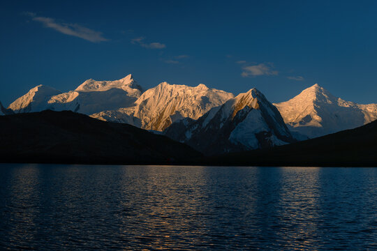 View of Rush Lake reflecting the snow-capped peaks of the Karakoram mountain range under a clear blue sky at sunset in Nagar Valley, Gilgit Baltistan, Pakistan.