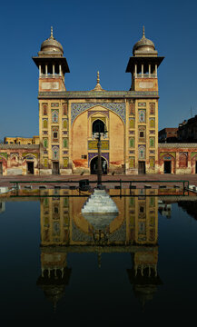 View of Wazir Khan Mosque with its intricate tile work, minarets, and reflection in the courtyard pool under a clear blue sky in Lahore, Punjab, Pakistan.