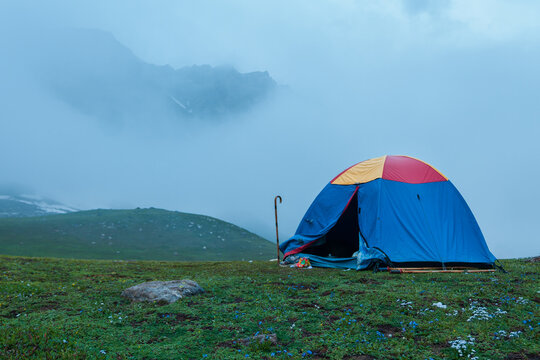 View of a colorful tent set up on a grassy mountain meadow with misty peaks in the background at Noori Top, Azad Kashmir, Pakistan.
